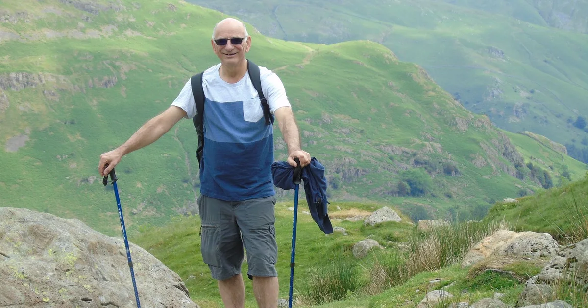 Smiling older man hiking a green mountain trail with trekking poles